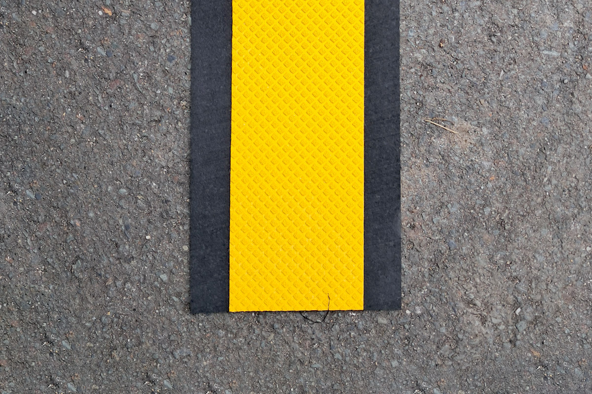 sagu®matting Fahrbahnmarkierungen (mobil) schwarzer Antirutschstreifen, darauf geklebt gelbes Fahrbahnmarkierungsband